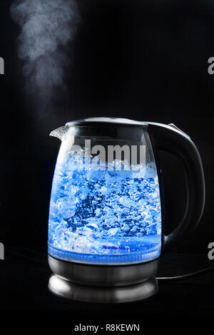 Siedepunkt Glas Wasserkocher mit blauem Licht auf einem schwarzen Hintergrund, Dampf kommt aus dem Auslauf. Stockfoto