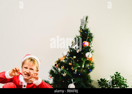 Toddler Boy mit lustigen Gesicht tragen Santa Kostüm versuchen, wie der Grinch Weihnachten, Ausdrücke und Konzepte auf isolierten weißen Hintergrund erschrecken. Stockfoto