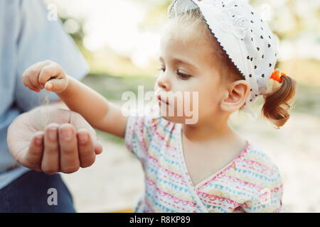 Ein kleines Mädchen gießt Sand in die Hand ihrer unkenntlich Vater. Das Konzept der Vergänglichkeit der Zeit und die Tatsache, dass die neuen Generationen der ol ersetzen Stockfoto