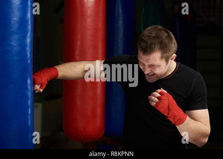 Kickboxer stanzen Sand bag. Ein kaukasischer Mann in rote Hand bandage Praxis kick Stockfoto