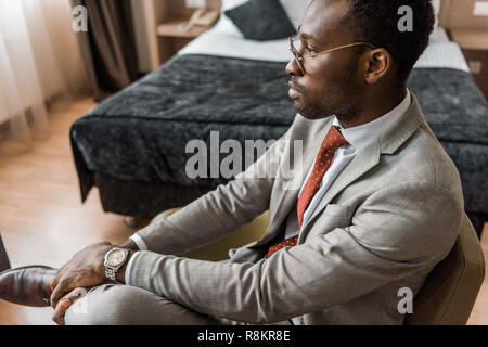 Nachdenklich afrikanische amerikanische Geschäftsmann in grauen Anzug im Hotel Zimmer sitzen Stockfoto