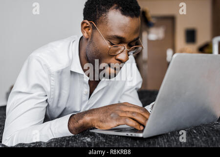 Afrikanische amerikanische Geschäftsmann in Gläsern Arbeiten am Laptop im Hotel Zimmer konzentriert Stockfoto