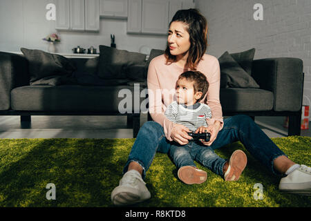 Kind und seine Mutter sitzen auf dem Boden und spielen video game mit Joystick zu Hause Stockfoto