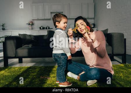 Attraktive Mutter, Spielzeug Dinosaurier zu ihrem kleinen Sohn im Wohnzimmer zu Hause Stockfoto