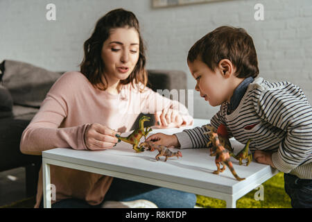 Fröhliche Frau und Sohn spielen Spielzeug Dinosaurier am Tisch im Wohnzimmer zu Hause Stockfoto