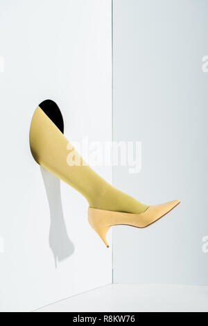 Zugeschnittenes Bild des Mädchens zeigt Bein in stilvollen gelbe Strumpfhosen und High Heel in Bohrung auf Weiß Stockfoto