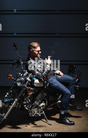 Hübscher Kerl in Sonnenbrille schiefen auf Motorrad in einer Garage. Stockfoto