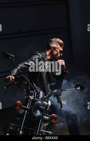 Classic Biker in Sonnenbrille sitzen auf dem Motorrad in einer Garage. Stockfoto