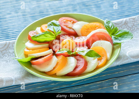 Grüne Platte mit traditionellen italienischen Caprese Salat auf Küchenpapier auf Blau Holztisch. Stockfoto