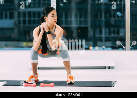 Attraktives asiatisches Mädchen tun hockt auf Fitness Matte zum Fitnessraum Stockfoto