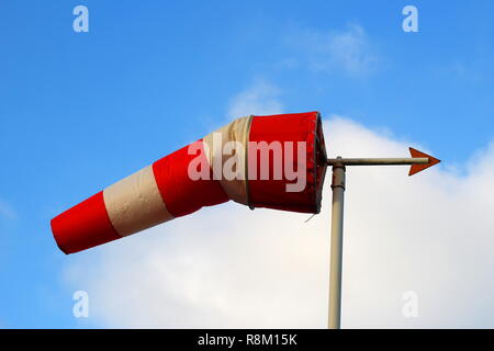 Eine rot-weiße Windsack mit einer Wetterfahne vor einem blauen Himmel mit weißen Wolken. Stockfoto