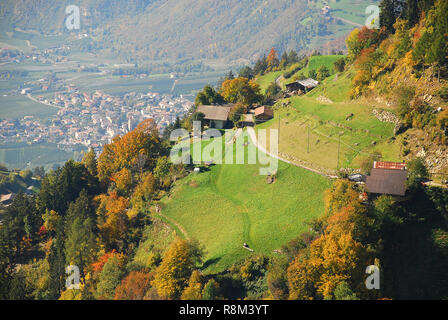 Blick auf Wiesen und Hütten in den italienischen Alpen in der Nähe von Meran, Südtirol, Italien. In der Ferne das Dorf Partschins Stockfoto