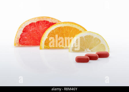 Grapefruit-, Orangen- und Zitronenscheiben mit drei Vitamin Tabletten. Natürliche Vitamine versus synthetische Tabletten Stockfoto