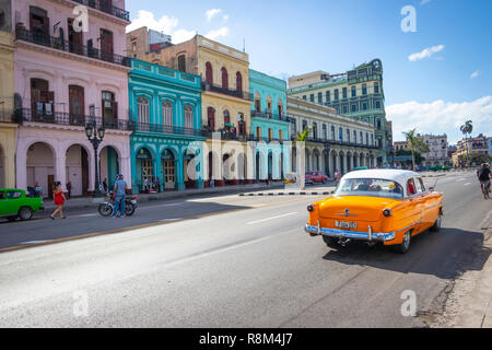 Ein Oldtimer fährt an farbenfrohen Kolonialgebäuden in einer sonnigen Straße vorbei und zeigt die lebendige Kultur und Architektur Havannas Stockfoto