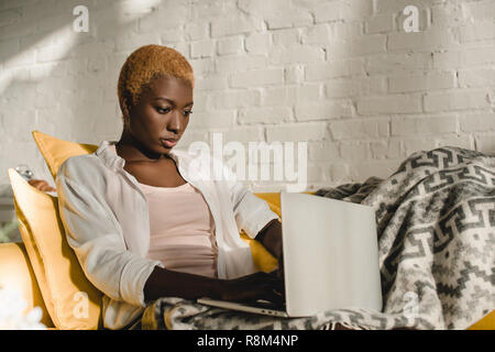 Afrikanische amerikanische Frau mit Laptop auf dem gelben Sofa gerichtet Stockfoto