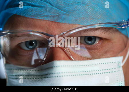 Stattliche männliche Arzt Gesicht durch das Tragen von schützender Maske Stockfoto