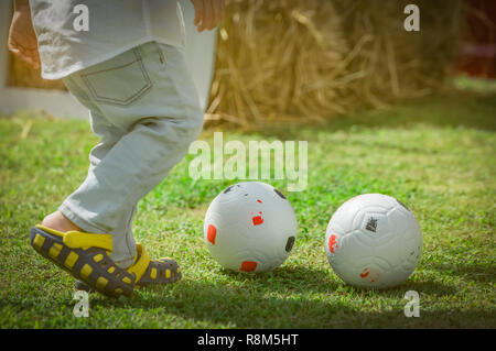 Glückliche kleine niedliche Junge spielt Fußball außerhalb zu Hause oder in der Schule im Sommer Tag. Vorschule Kinder spielen Fußball in der grüne Rasen. Kind mit casual Schuhe pl Stockfoto