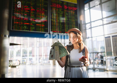 Thema Reisen und Transport. Schönen jungen kaukasischen Frau in Kleid und Rucksack im Bahnhof Terminal mit Blick auf elektronische sc Stockfoto