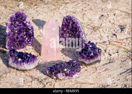 1 Rosenquarz Edelstein umgeben von 5 amethyst Kristalle am Strand und im Gras Stockfoto