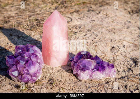 1 Rosenquarz Edelstein zusammen mit 2 amethyst Kristalle am Strand und im Gras Stockfoto