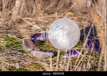 Weißen Quarz ball von Amethyst Kristalle mit in das Gras umgeben Stockfoto