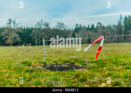 Schönes Bild von einer Wiese mit Holzstangen und Kabel mit rotem Klebeband an einem bewölkten Tag und mit Winter Dunst in den Belgischen Ardennen Stockfoto
