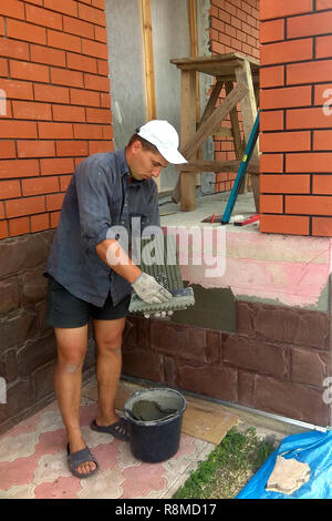 Der Prozess der Installation von Sandstein dekorative Fliesen auf dem Fundament des Hauses 2018 Stockfoto