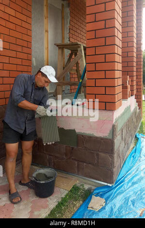 Der Prozess der Installation von Sandstein dekorative Fliesen auf dem Fundament des Hauses 2018 Stockfoto