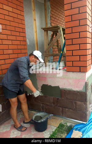 Der Prozess der Installation von Sandstein dekorative Fliesen auf dem Fundament des Hauses 2018 Stockfoto