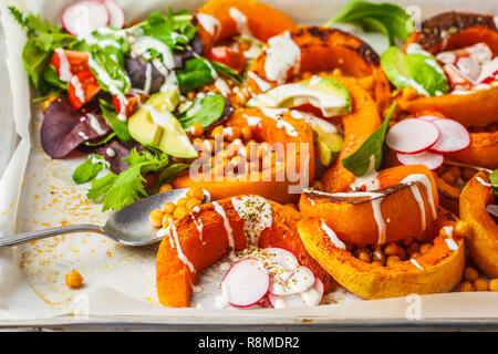 Gebackener Kürbis mit Kichererbsen auf ein Backblech mit Avocado, Tahini und Gemüse. Stockfoto