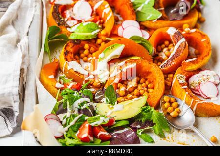 Gebackener Kürbis mit Kichererbsen auf ein Backblech mit Avocado, Tahini und Gemüse. Stockfoto