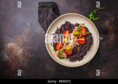 Schwarzer Reis Nudeln mit Thunfisch, Tomaten und Oliven in eine weiße Platte, dunklen Hintergrund. Stockfoto