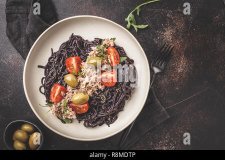 Schwarzer Reis Nudeln mit Thunfisch, Tomaten und Oliven in eine weiße Platte, dunklen Hintergrund. Stockfoto