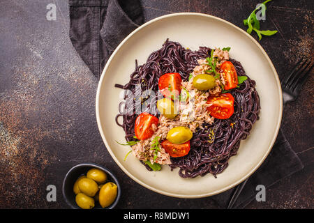 Schwarzer Reis Nudeln mit Thunfisch, Tomaten und Oliven in eine weiße Platte, dunklen Hintergrund. Stockfoto