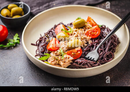 Schwarzer Reis Nudeln mit Thunfisch, Tomaten und Oliven in eine weiße Platte, dunklen Hintergrund. Stockfoto