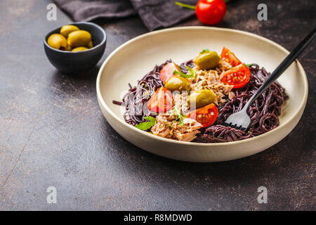 Schwarzer Reis Nudeln mit Thunfisch, Tomaten und Oliven in eine weiße Platte, dunklen Hintergrund. Stockfoto