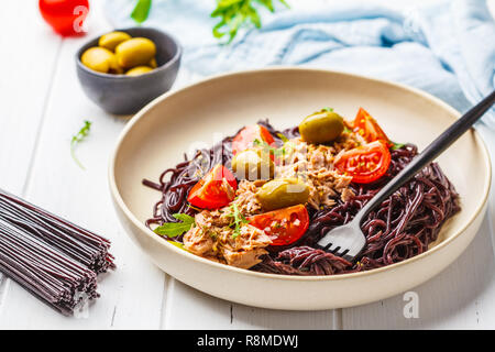 Schwarzer Reis Nudeln mit Thunfisch, Tomaten und Oliven in eine weiße Platte auf weißem Holz- Hintergrund. Stockfoto