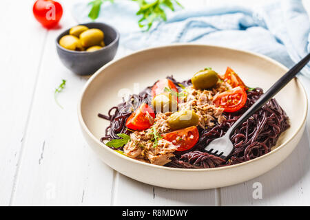 Schwarzer Reis Nudeln mit Thunfisch, Tomaten und Oliven in eine weiße Platte auf weißem Holz- Hintergrund. Stockfoto