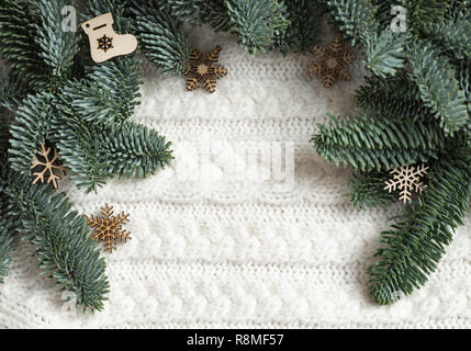 Holz- Weihnachtsschmuck liegen in der Nähe der Tannenzweigen auf einem weißen Strickpullover Stockfoto