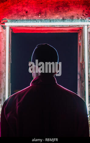 Männliche stand vor einer geheimnisvollen Tür. Das Gebäude ist hell rot und sehr dunkel. Stockfoto