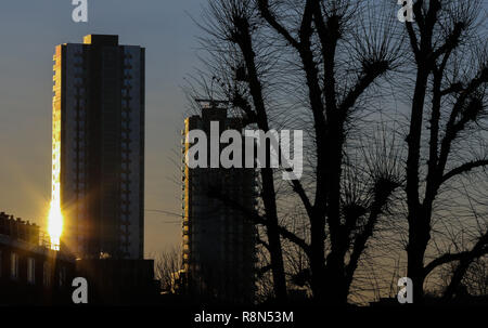 London, Großbritannien. 17 Dez, 2018. Eine Reflexion der Sonnenstrahlen in Windows und ein hoher Turmblock Silhouette von Bäumen Äste sind während eines Winters Golden Sun Rise in London gesehen. Credit: Dinendra Haria/SOPA Images/ZUMA Draht/Alamy leben Nachrichten Stockfoto