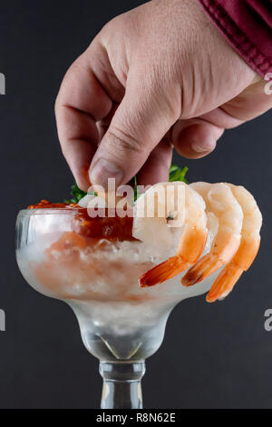 Des Menschen Hand tauchen eine Garnele in Cocktailsauce. Der dunkle Hintergrund. Garnelen hing an der Seite des margarita Glas. Stockfoto