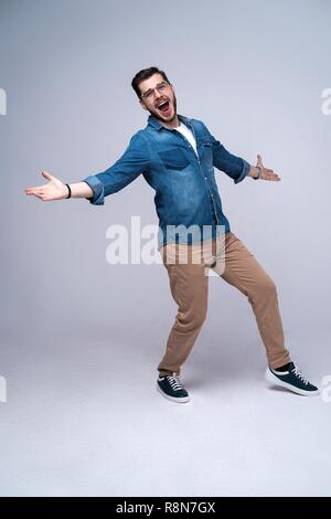 Vertikale Bild von schockiert Mann im Hemd und Jeans. Auf grauem Hintergrund Stockfoto