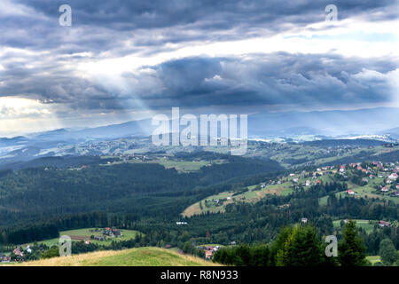 Sonnenstrahlen durch die Wolken über dem Schlesischen Beskiden. Blick auf Koniakow Dorf von der Spitze des Ochodzita Berg. Polen, Europa Stockfoto