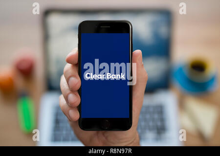 Ein Mann schaut auf seinem iPhone die zeigt die ClearBank Logo (nur redaktionelle Nutzung). Stockfoto