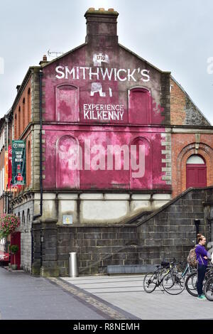 Blick auf die Straße von Kilkenny mit Wandmalereien Werbung von Kilkenny Brauerei Besichtigung und Verkostung auf Mauer bis zum Schornstein. Stockfoto