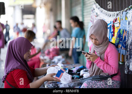 Zwei Philippinische moslemischen Mädchen verkauf Socken auf einer Seitengasse, eines der Mädchen über ein Mobiltelefon, Cebu City, Philippinen Stockfoto