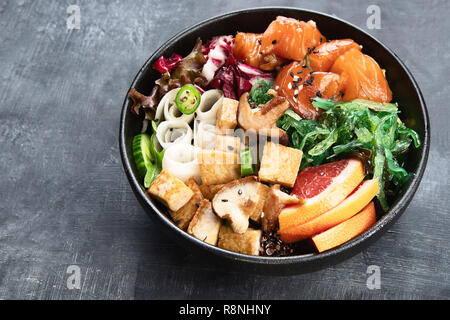 Poke Schüssel mit Lachs, guinoa, Gemüse, Obst und Tofu auf dunklem Hintergrund Stockfoto