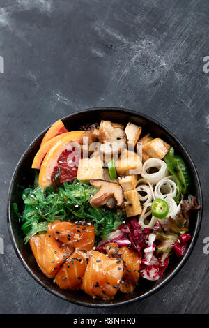 Poke Schüssel mit Lachs, guinoa, Gemüse, Obst und Tofu auf dunklem Hintergrund Stockfoto