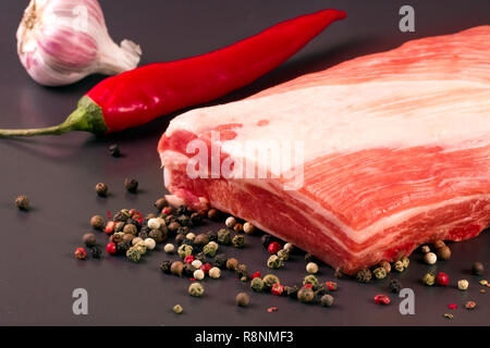 Stück Schweinefleisch auf einem dunklen Hintergrund mit Pfeffer und Chili Stockfoto